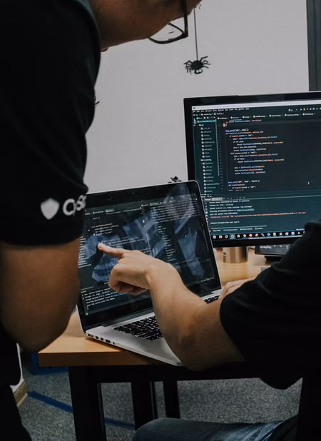 Two engineers reading code together on a laptop, one pointing at the screen.